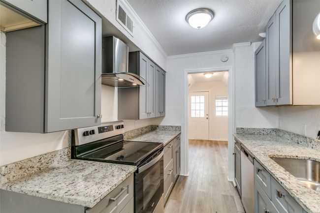 Kitchen with wall chimney range hood, a sink, light wood-type flooring, stainless steel appliances, and visible vents | Image 8