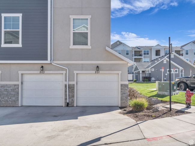View of property with stone siding, a residential view, a garage, concrete driveway, and stucco siding | Image 17