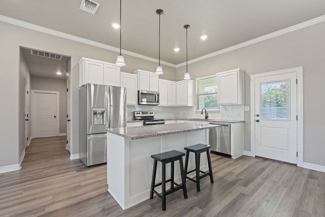Kitchen featuring appliances with stainless steel finishes, a center island, tasteful backsplash, wood finished floors, and ornamental molding | Image 10