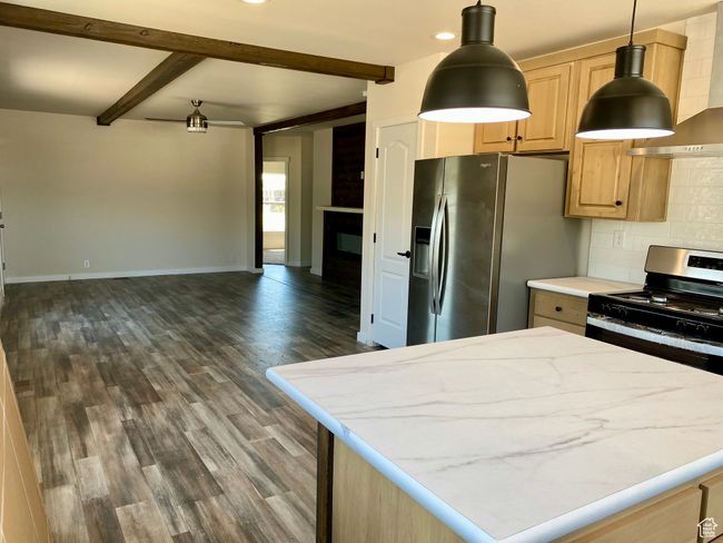 Kitchen featuring appliances with stainless steel finishes, beamed ceiling, decorative backsplash, open floor plan, and wall chimney range hood | Image 7