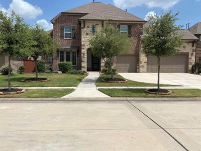 This is a two-story brick home featuring a well-manicured lawn with two trees, a walkway to the front door, and a three-car garage. | Image 2