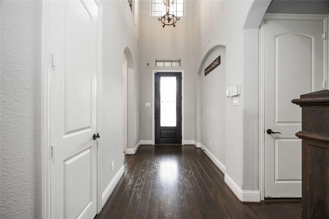 This entryway features high ceilings, dark hardwood floors, and light-colored walls. It includes elegant archways, white doors, and a decorative chandelier, creating a welcoming and spacious atmosphere. | Image 4