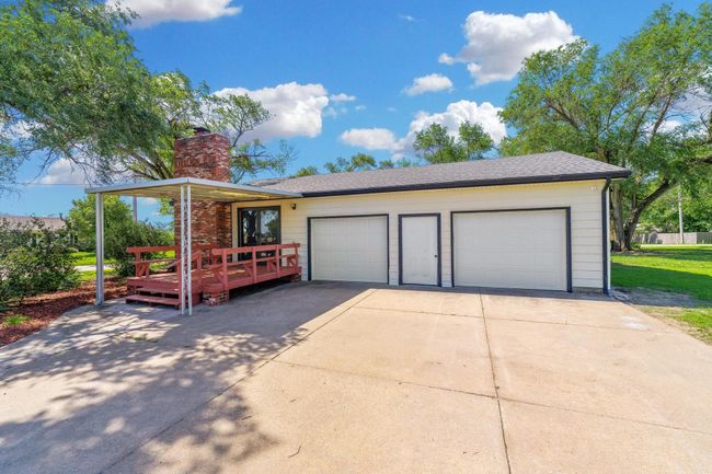 View of front of property with concrete driveway, a chimney, a wooden deck, and roof with shingles | Image 27