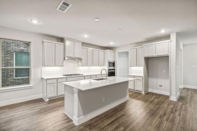 Kitchen featuring stainless steel appliances, dark hardwood / wood-style flooring, white cabinetry, sink, and an island with sink | Image 2