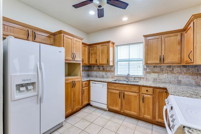 Kitchen with white appliances, a ceiling fan, backsplash, light tile patterned flooring, and brown cabinets | Image 14