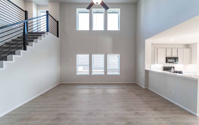 Unfurnished living room with a high ceiling, a ceiling fan, stairway, and light wood-type flooring | Image 4