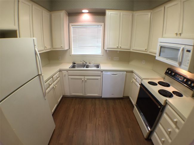 Kitchen with white cabinets, white appliances, a sink, and dark wood finished floors | Image 4