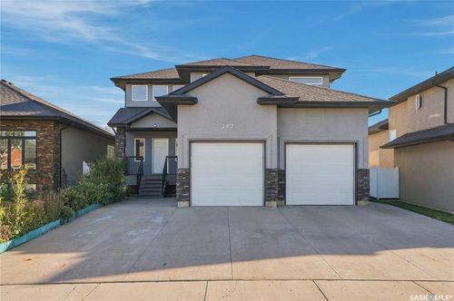 Two-story stucco and stone exterior featuring multiple windows, a prominent entrance with steps, and a dual garage | Card Image