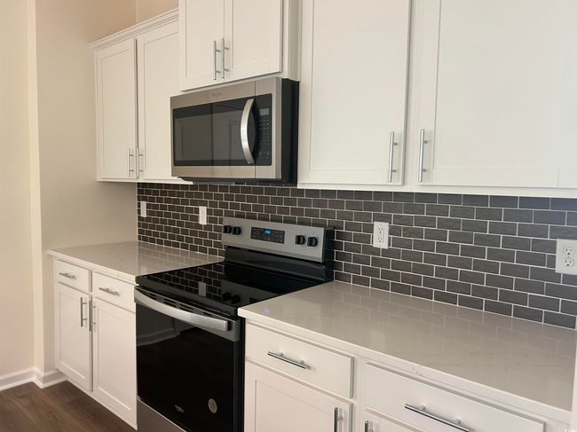 Kitchen with appliances with stainless steel finishes, dark wood-style floors, light stone counters, white cabinets, and backsplash | Image 7