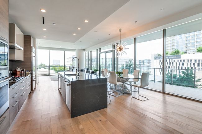 Kitchen featuring modern cabinets, light wood finished floors, built in appliances, a spacious island, and a wall of windows | Image 4