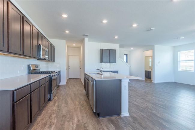 Kitchen with appliances with stainless steel finishes, tasteful backsplash, light wood finished floors, light countertops, and dark brown cabinets | Image 17