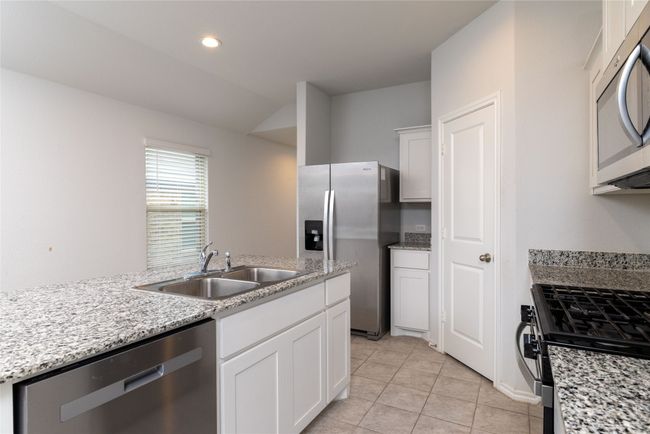 Kitchen with stainless steel appliances, a sink, white cabinetry, light tile patterned floors, and light stone countertops | Image 9