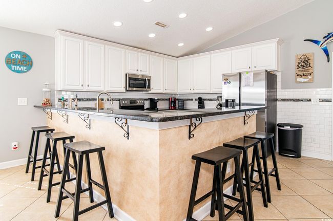 Kitchen with stainless steel appliances, light tile patterned floors, a peninsula, a kitchen breakfast bar, and lofted ceiling | Image 26