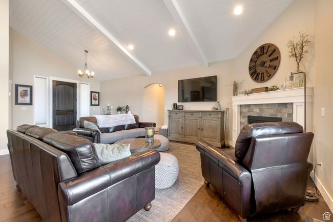 Living area featuring an inviting chandelier, lofted ceiling with beams, a fireplace, arched walkways, and wood finished floors | Image 10