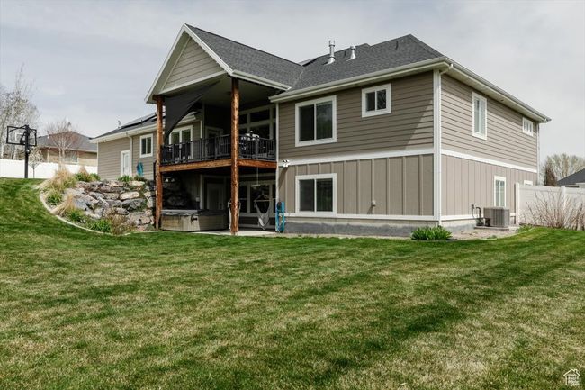 Back of property featuring a balcony, board and batten siding, fence, a hot tub, and a yard | Image 69