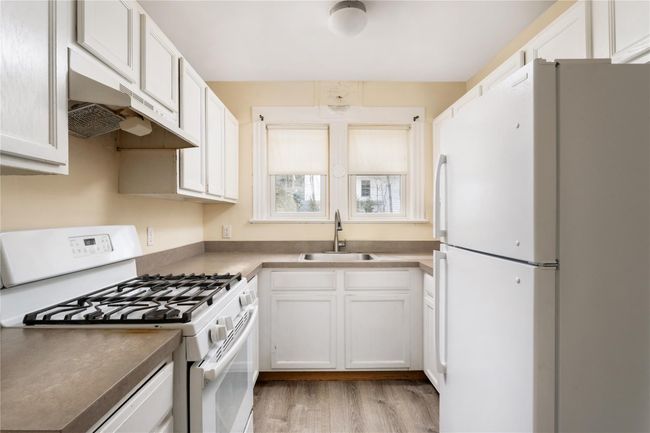 Kitchen with white cabinets, under cabinet range hood, a sink, white appliances, and light wood-style floors | Image 7