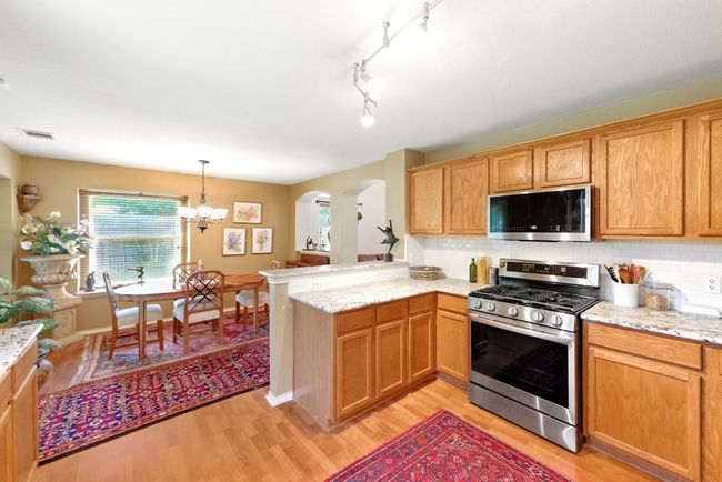Kitchen featuring stainless steel appliances, light wood-type flooring, arched walkways, a peninsula, and tasteful backsplash | Image 14