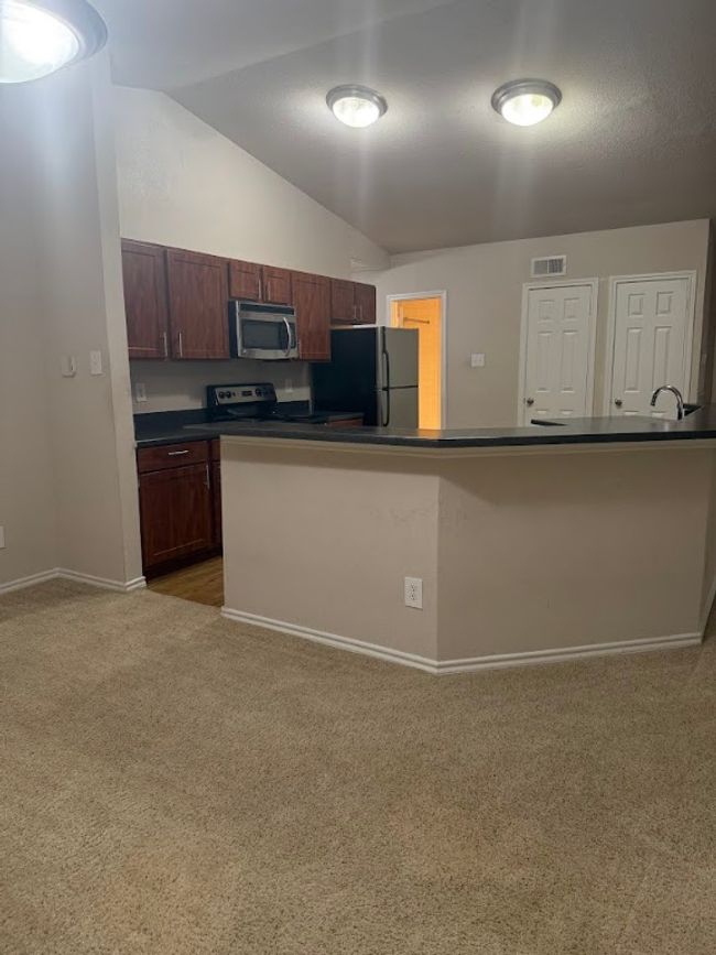 Kitchen featuring appliances with stainless steel finishes, vaulted ceiling, light carpet, and dark countertops | Image 12