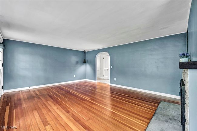 Unfurnished room with arched walkways, hardwood flooring, and a stone fireplace | Image 4