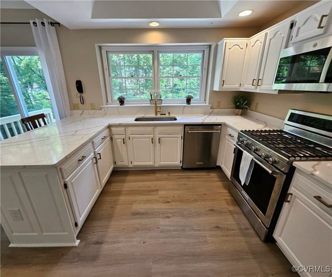 Kitchen with stainless steel appliances, a peninsula, light quartz countertops, white cabinetry, and crown molding & LVP flooring | Image 18