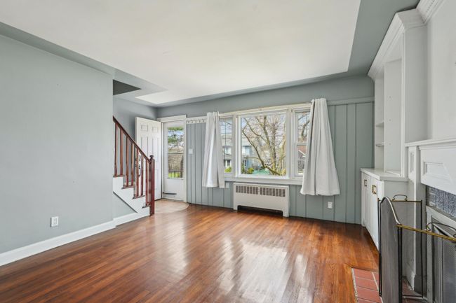 Unfurnished living room with baseboards, a fireplace with flush hearth, wood finished floors, radiator heating unit, and stairs | Image 6