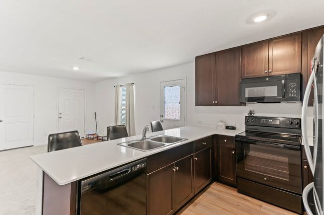Kitchen with black appliances, a peninsula, light countertops, dark brown cabinets, and recessed lighting | Image 18