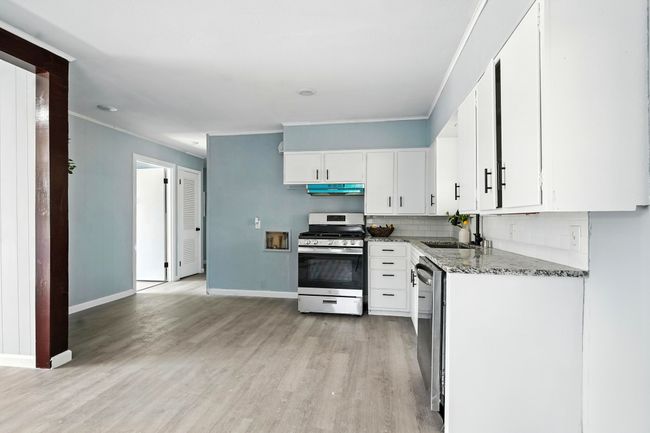 Kitchen with stainless steel appliances, under cabinet range hood, light wood finished floors, stone countertops, and white cabinets | Image 10