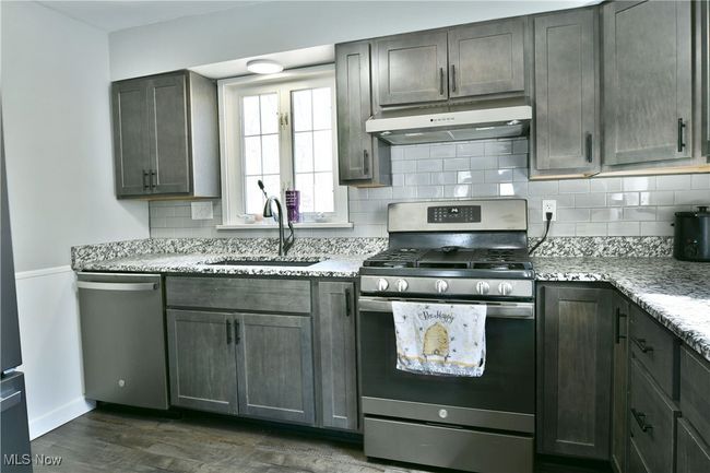 Kitchen featuring backsplash, a sink, dark wood finished floors, under cabinet range hood, and stainless steel appliances | Image 17