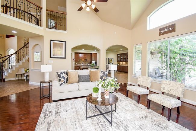 With soaring ceilings and two-story windows, this living area feels both expansive and warm. A fireplace adds a central focal point, while dual archways open to the kitchen, reinforcing the home’s natural flow. | Image 11