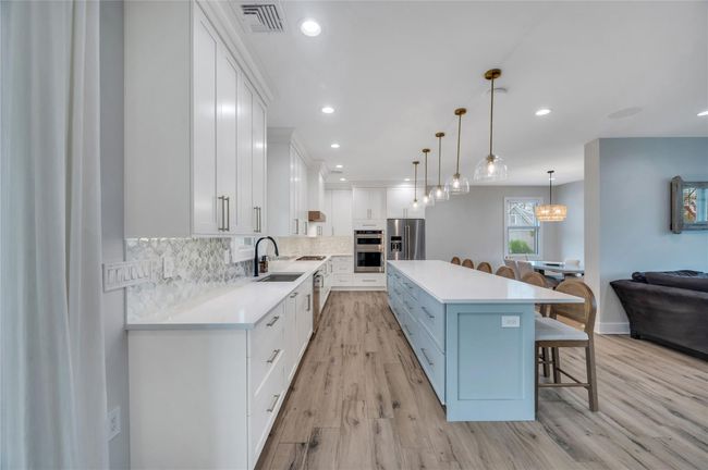 Kitchen featuring light wood-style flooring, a breakfast bar, appliances with stainless steel finishes, white cabinetry, and backsplash | Image 14
