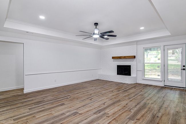 Unfurnished living room with a tray ceiling, ornamental molding, wood finished floors, a brick fireplace, and a ceiling fan | Image 12