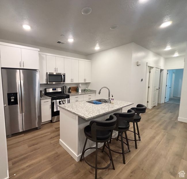 Kitchen featuring stainless steel appliances, a sink, light wood finished floors, a breakfast bar, and white cabinets | Image 6