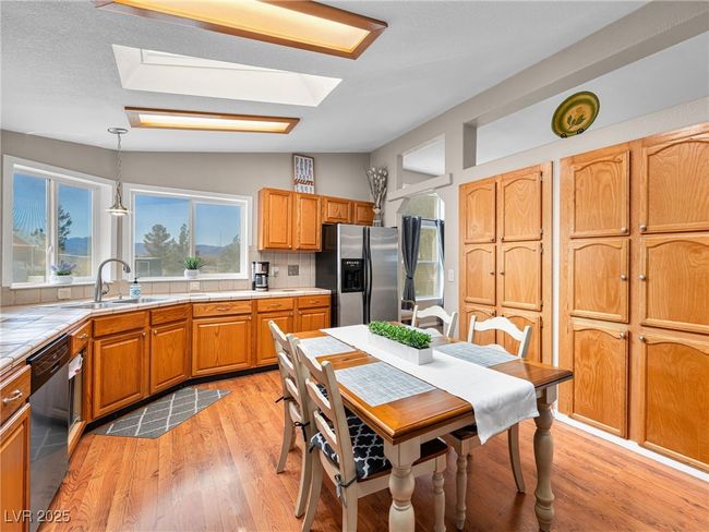 Kitchen featuring dishwashing machine, tile countertops, vaulted ceiling with skylight, stainless steel fridge with ice dispenser, and a sink | Image 24