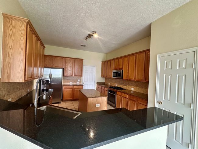 Kitchen featuring stainless steel appliances, backsplash, a center island, a peninsula, and a textured ceiling | Image 8