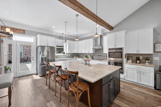 Kitchen featuring appliances with stainless steel finishes, white cabinetry, a kitchen bar, backsplash, and a center island | Image 14