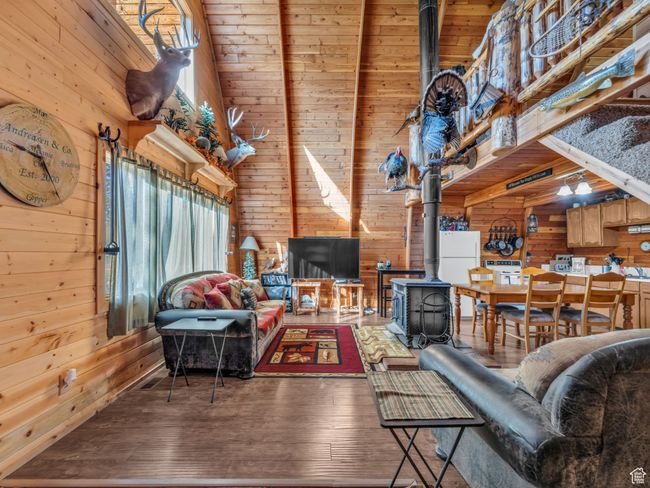 Living room with wood walls, a wood stove, a high ceiling, and hardwood / wood-style flooring | Image 6