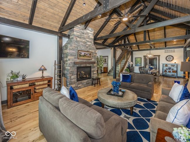 living area with a stone fireplace, stairs, wood ceiling with exposed beams, wood-type flooring, and high vaulted ceiling | Image 8