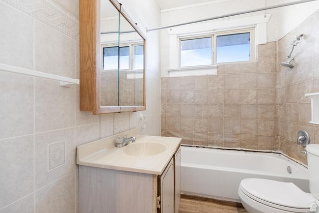 Full bathroom with tile walls, toilet, wood finished floors, vanity, and shower / washtub combination | Image 15