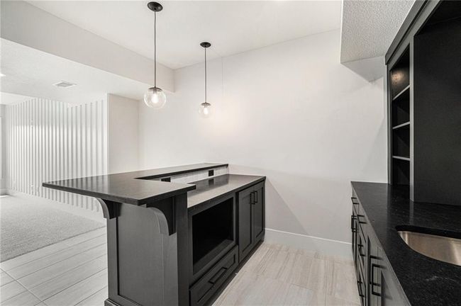 Kitchen featuring dark cabinets, baseboards, a breakfast bar area, decorative light fixtures, and dark stone countertops | Image 27