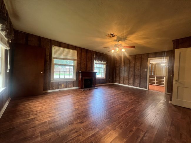 Living room with a ceiling fan and dark wood-type flooring, and wooden walls | Image 4