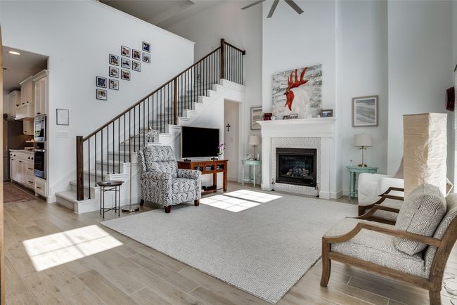 Living room with a high ceiling, stairway, light wood-style floors, and a glass covered fireplace | Image 5