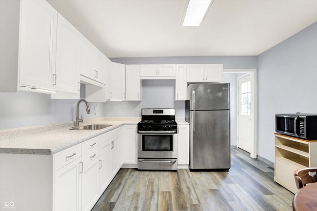 kitchen with stainless steel appliances, a sink, light wood-style floors, and white cabinetry | Image 8