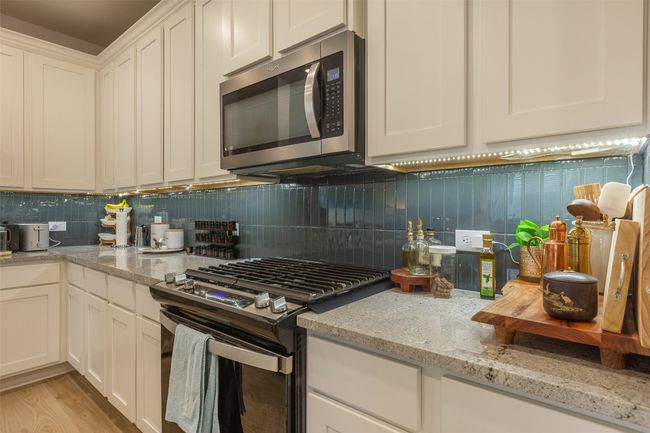 Kitchen with stainless steel appliances, backsplash, white cabinetry, light stone countertops, and light wood-type flooring | Image 12