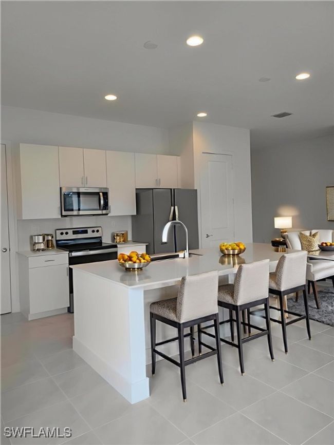 Kitchen featuring stainless steel appliances, a breakfast bar, recessed lighting, light countertops, and a kitchen island with sink | Image 6
