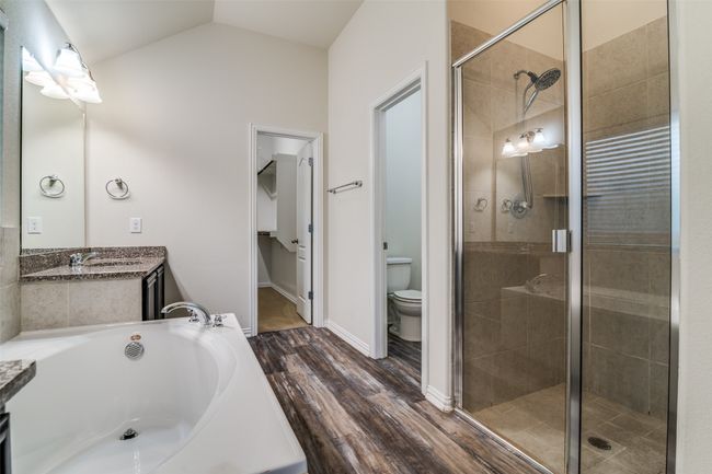 Primary bathroom featuring a stall shower, vanity, a garden tub, wood finished floors, and vaulted ceiling | Image 16
