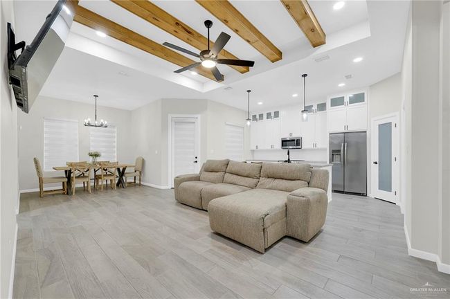 Living room with baseboards, wood-style tile flooring, ceiling fan with notable chandelier, and a tray ceiling | Image 8