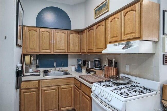 Kitchen with a sink, under cabinet range hood, backsplash, light countertops, and white range with gas stovetop | Image 4