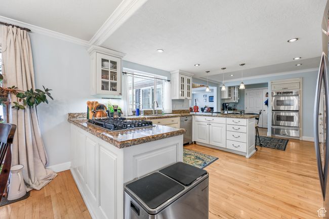 Kitchen featuring crown molding, stainless steel appliances, light wood-style flooring, glass insert cabinets, and a peninsula | Image 11