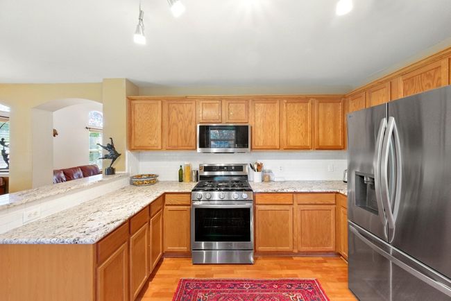 Kitchen with stainless steel appliances, light wood-style flooring, a peninsula, arched walkways, and light stone countertops | Image 13