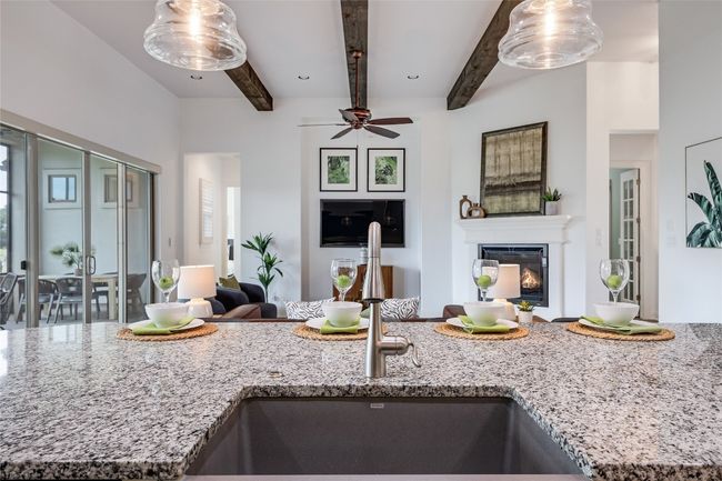 Kitchen featuring open floor plan, beamed ceiling, light stone counters, a glass covered fireplace, and ceiling fan | Image 7